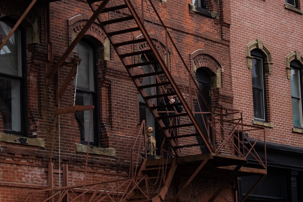 Man smoking cigarette at a fire escape on side of building.